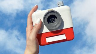 Poesi-kameraet i rødt og hvidt, i hånden med blå himmel som baggrund.