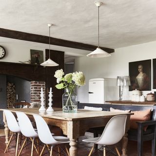 white pendant lights over wooden dining table with white chairs and black ceiling beams