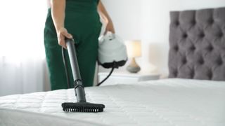 A woman cleans a mattress with a vacuum cleaner to remove pollen, a hayfever allergen