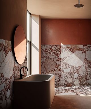 bathroom with walls featuring large slabs of dark red and white marble panels which extends onto the floor, large stone freestanding bath and red painted walls above the panels