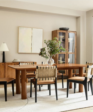 A brown wooden dining table with rattan chairs with a rug underneath, a console table and cupboard next to it, and gray walls and flooring