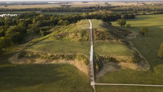 Aerial view of green hilltop with staircases and trees and river in background