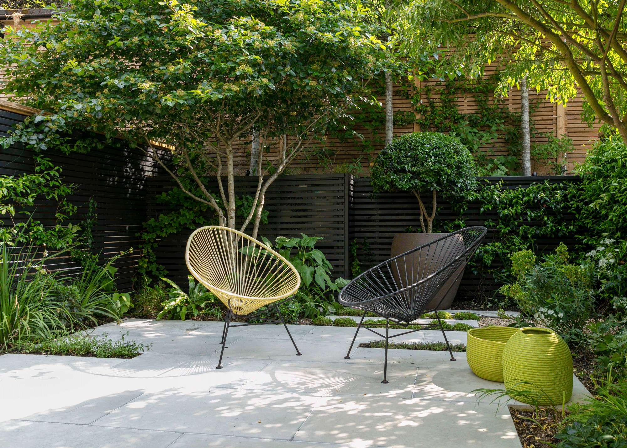 small paved patio with trees and other planting, chairs