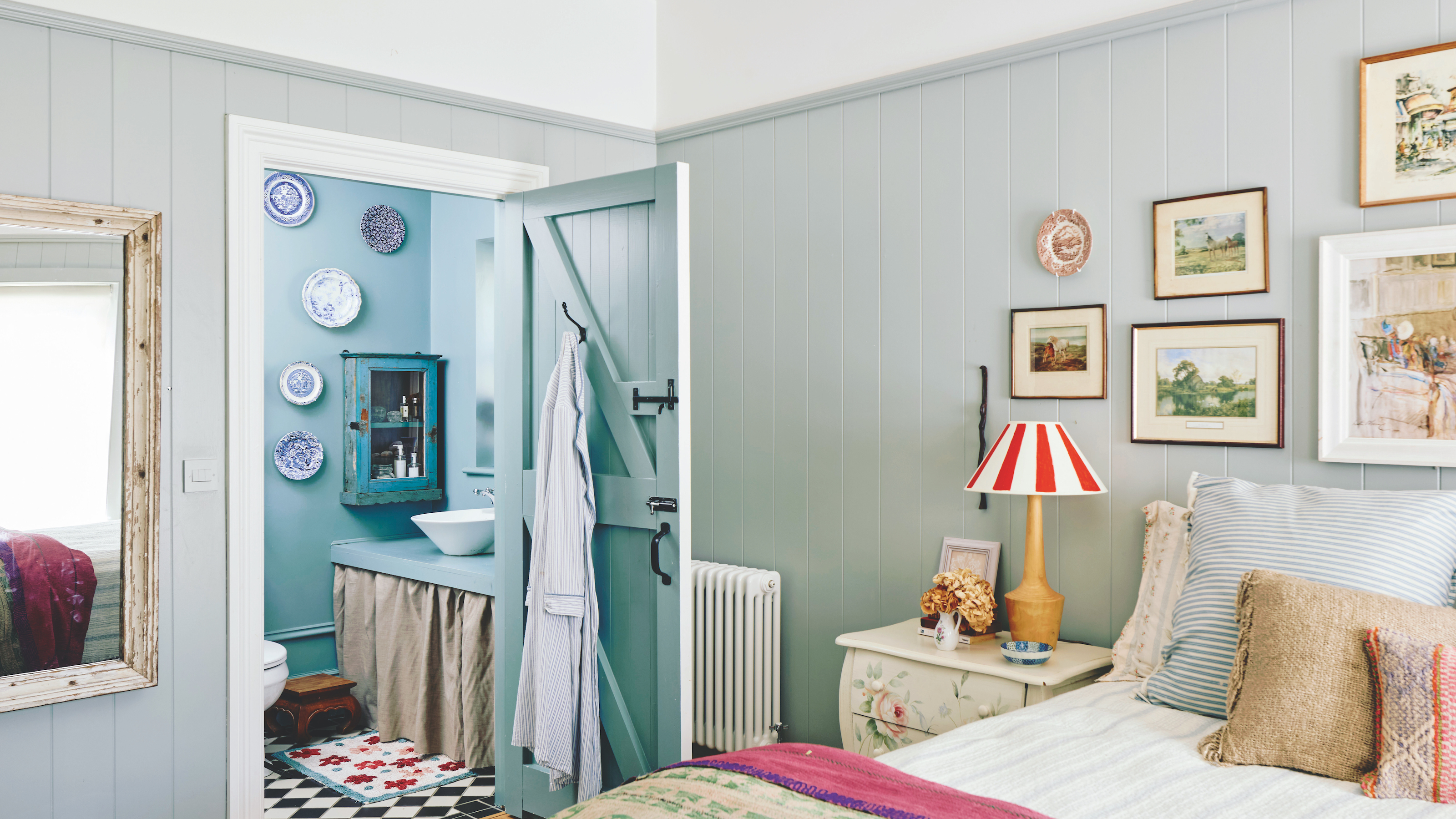 bedroom with tongue and groove wooden planelling and picture gallery wall above bed with view to ensuite blue bathroom