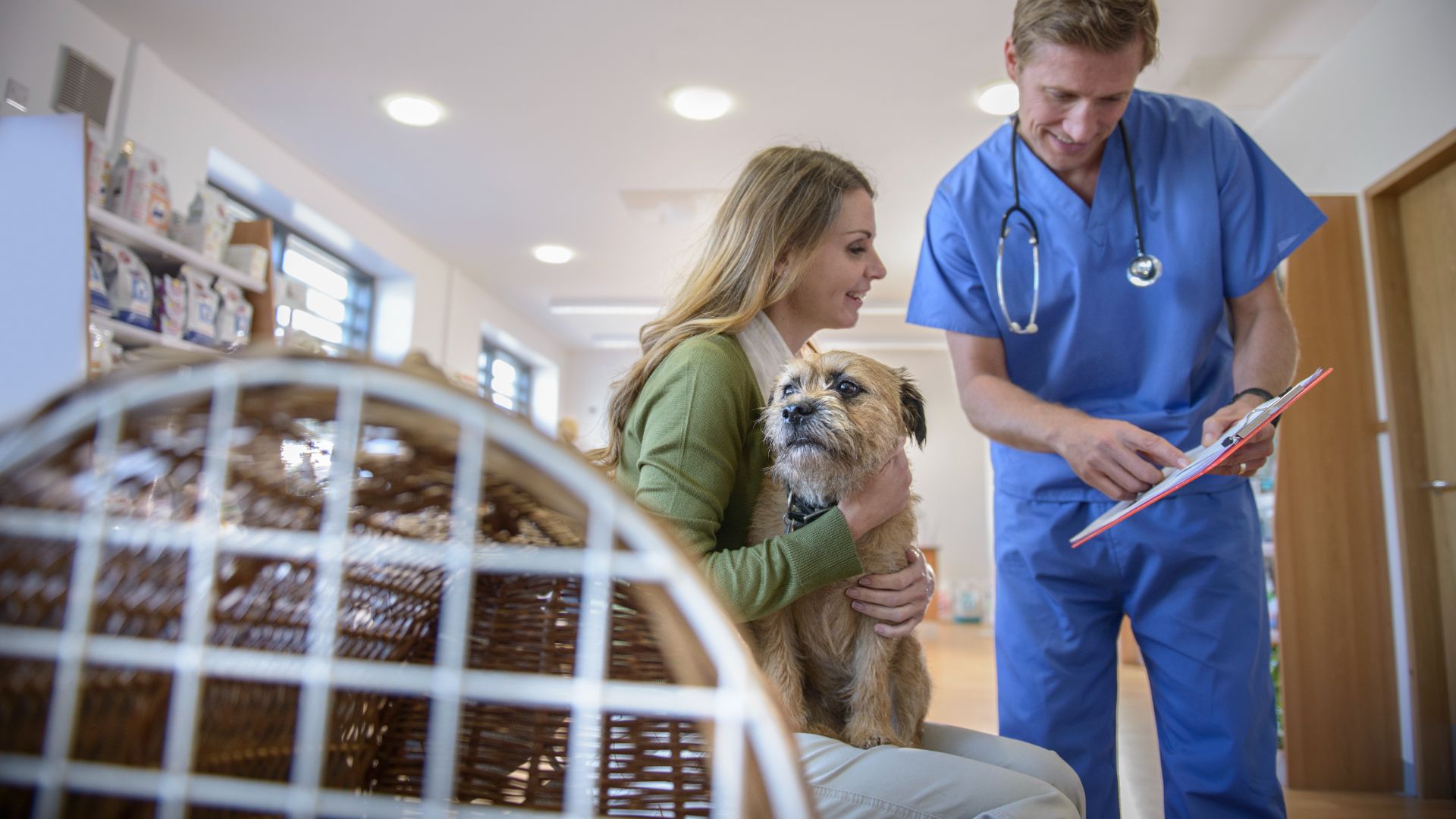 woman with dog on lap engaged in conversation with a vet, who's gesturing to a clipboard