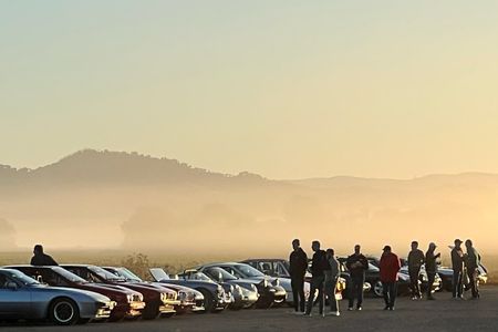 Morning at a classic car event in Northern California, with a mountain view behind classic cars lined up. It is foggy and people are milling about, looking at the cars.