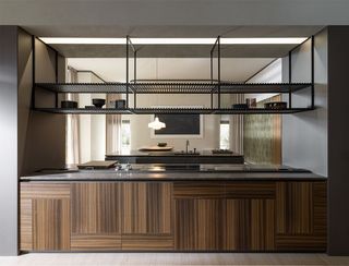 A kitchen with expressive wooden cabinets and an open plan design featuring black metal open storage at the top