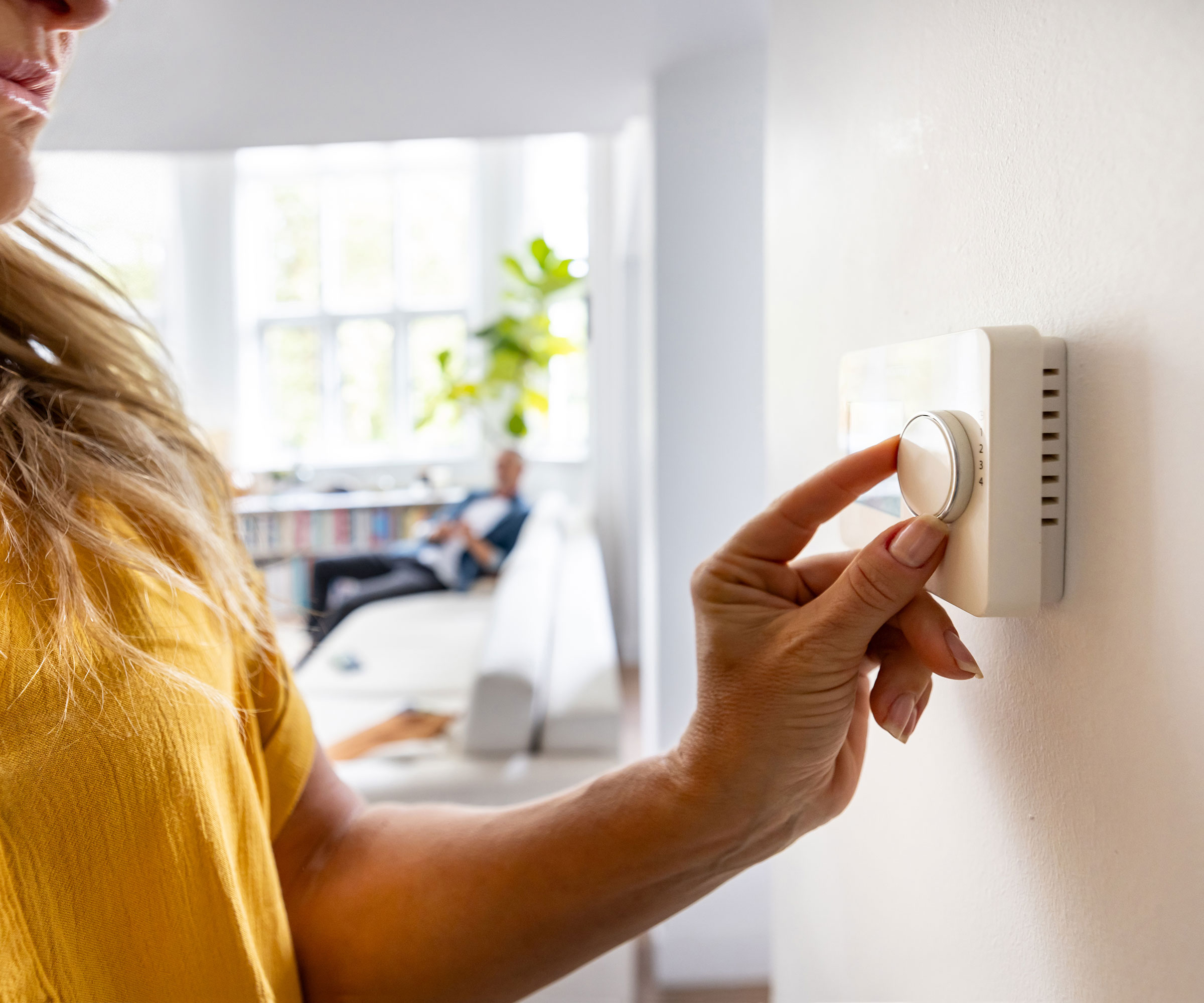 woman in yellow top adjusting thermostat