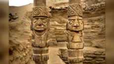 Two wooden staffs with carvings depicting people wearing headgear.