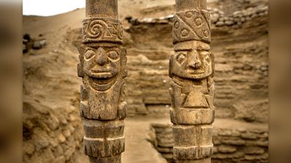 Two wooden staffs with carvings depicting people wearing headgear.