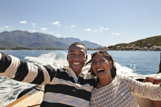 Happy young couple taking selfie while enjoying boat ride on sunny day