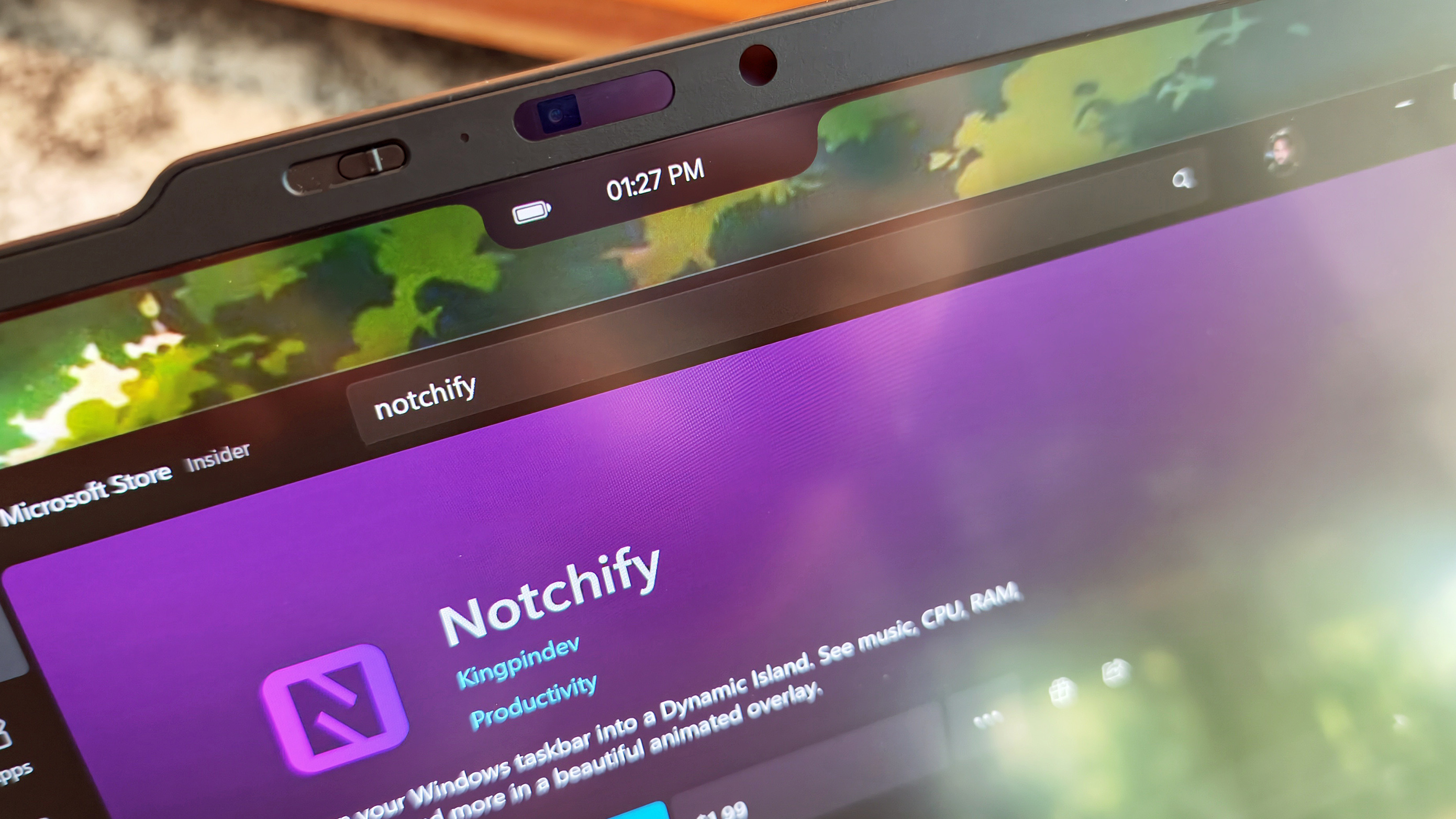 Close-up of a laptop screen showing a black notch overlay with a battery icon and time display above the Microsoft Store page for the Notchify app.