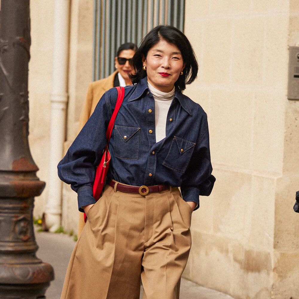Woman wearing a denim button down, pleated shorts, white turtleneck, and a red bag