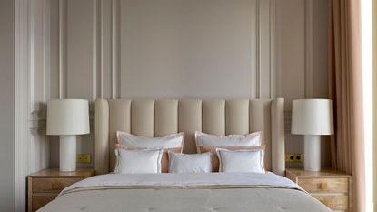 A neutral bedroom with a large upholstered cream headboard and matching cream bedding