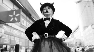 Black-and-white image, showing a woman in the streets, wearing a hat and clown makeup