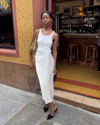 Sylvie Mus wearing a white tank top, white skirt, brown bag, and black Manolo Blahnik heels.