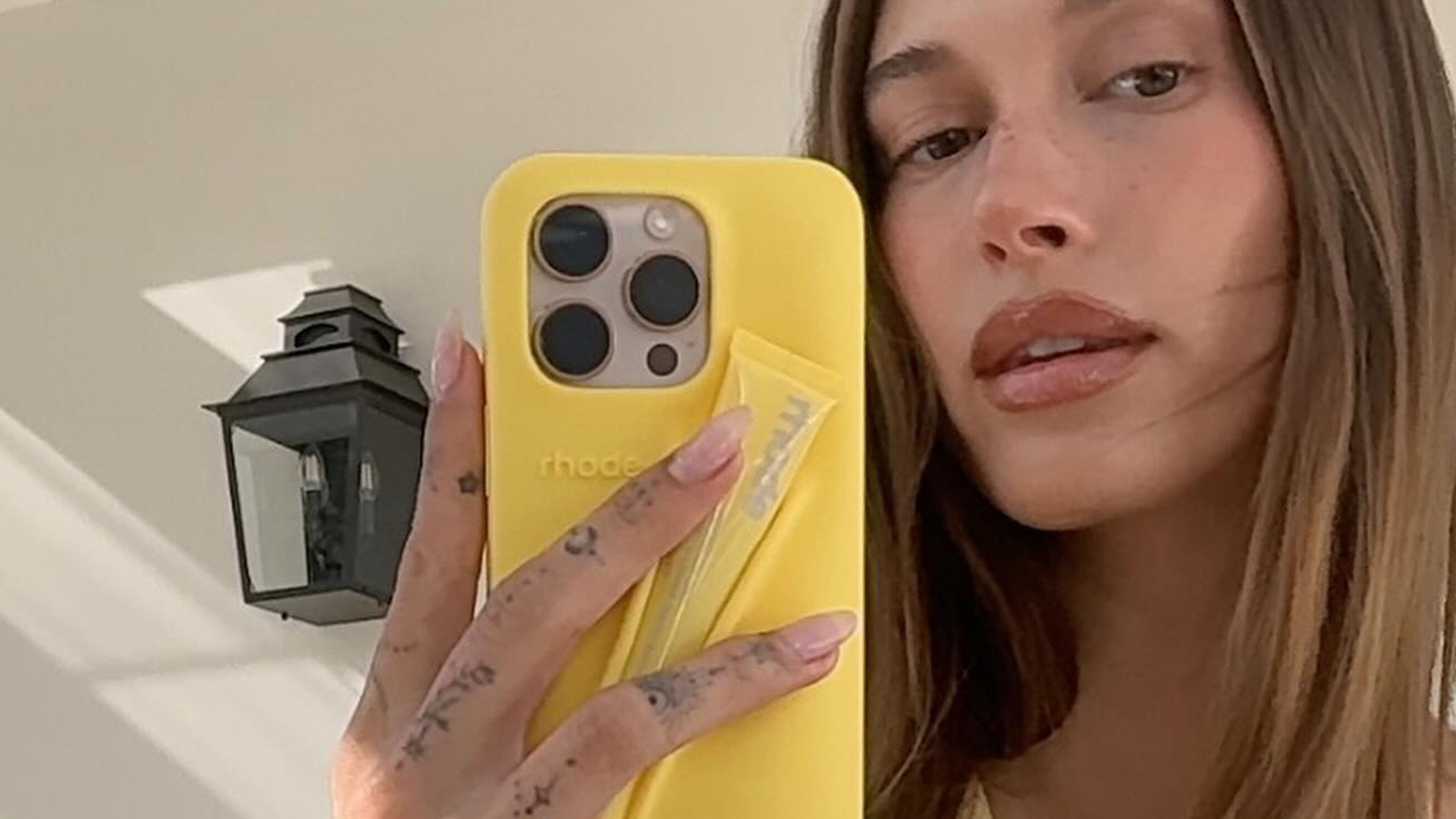 Hailey holds the lemon yellow rhode phone case and peptide lip.