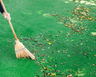 A gardener sweeps fallen leaves on fake grass with a wooden broom