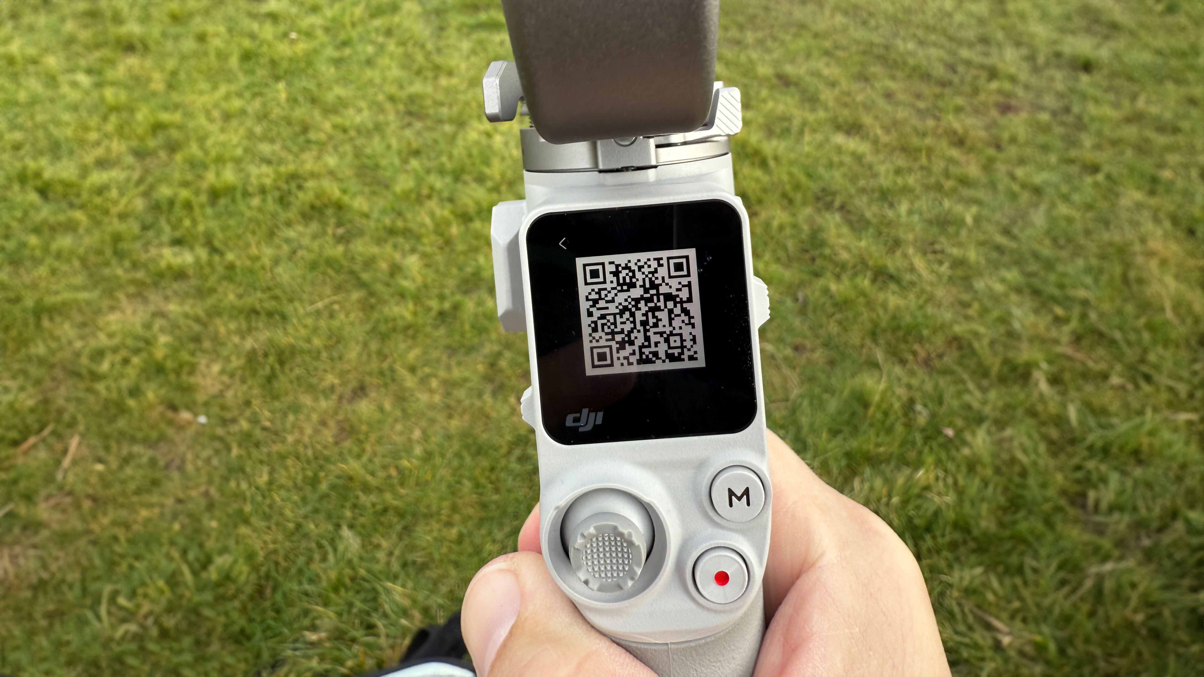 The QR code on screen for pairing the DJI RS 4 Mini held in hand with grass behind