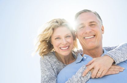 Cheerful Woman Embracing Man From Behind Against Sky