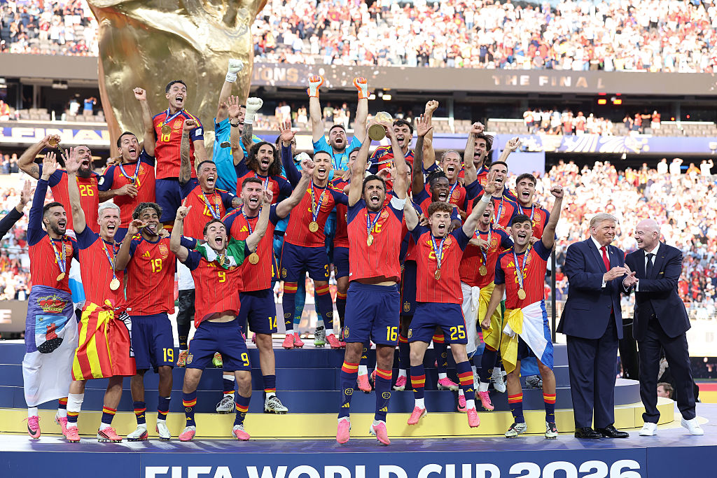 Rodri of Spain celebrates by lifting the FIFA World Cup trophy with teammates as Gianni Infantino, president of FIFA, and Donald Trump, president of the USA, also stand on the podium