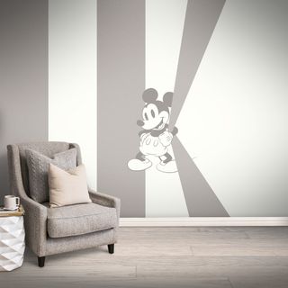 room with mickey mouse on wall and grey chair with cushions