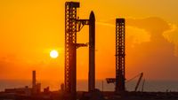 A towering SpaceX Starship rocket stands at Starbase's Pad 2, silhouetted against a yellow sky and rising sun.