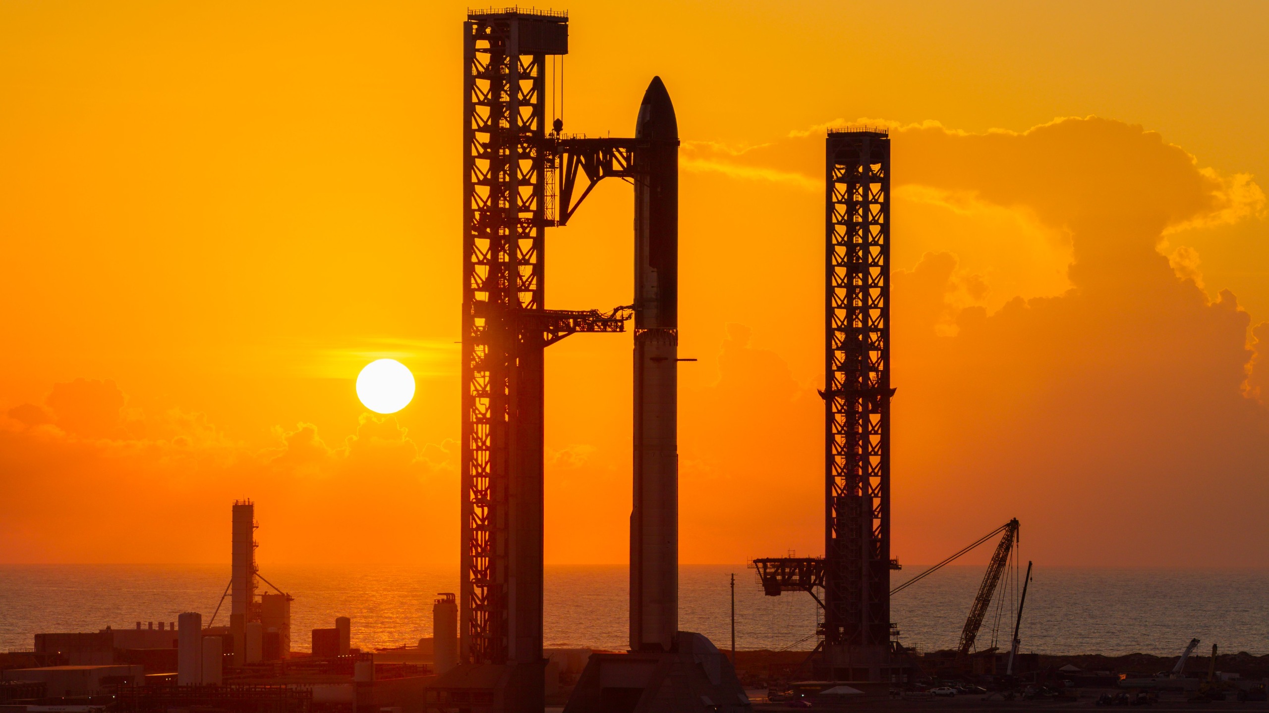 A towering SpaceX Starship rocket stands at Starbase's Pad 2, silhouetted against a yellow sky and rising sun.