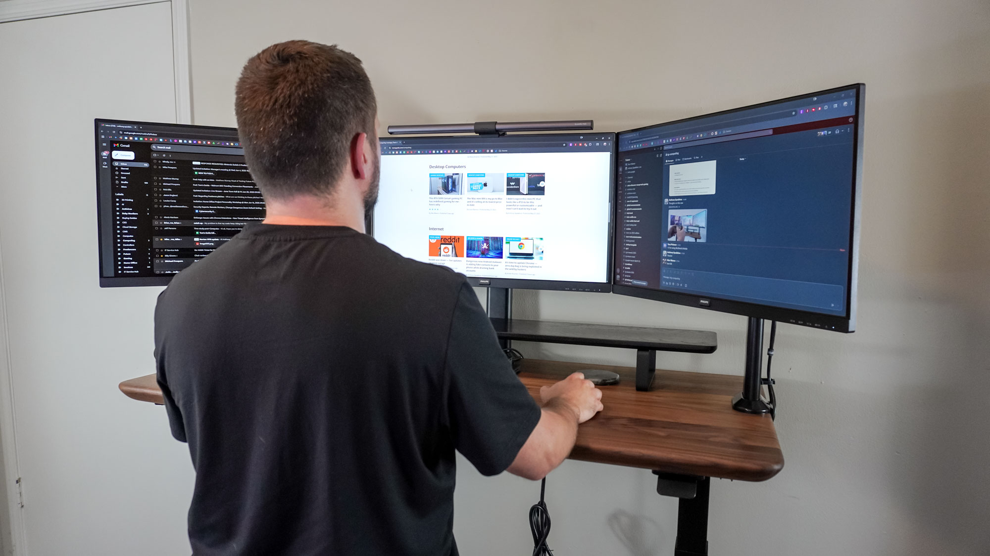 A person working at a standing desk using a triple monitor setup