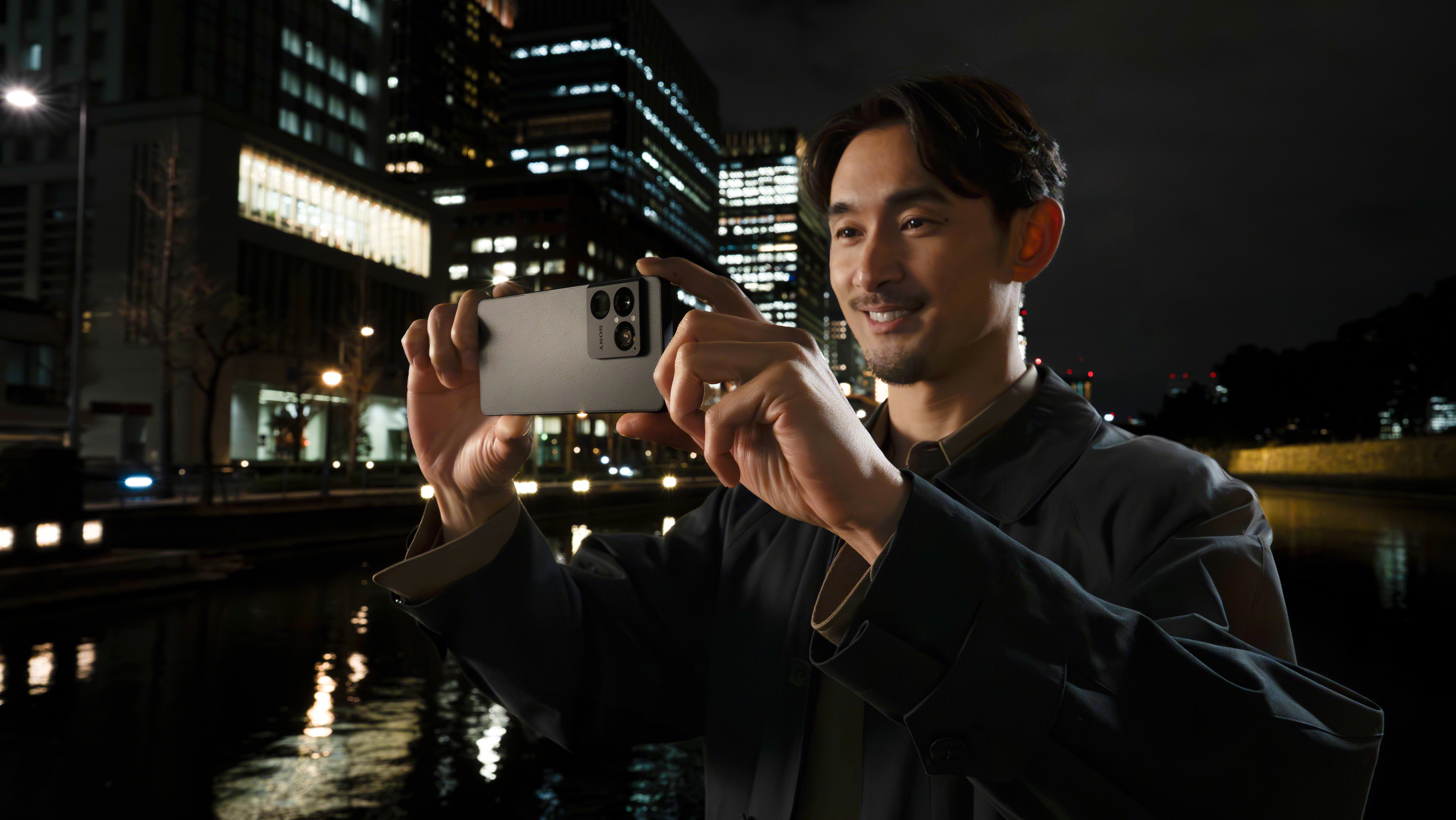 Sony Xperia 1 VIII held up by a person taking a photo in front of a nighttime cityscape