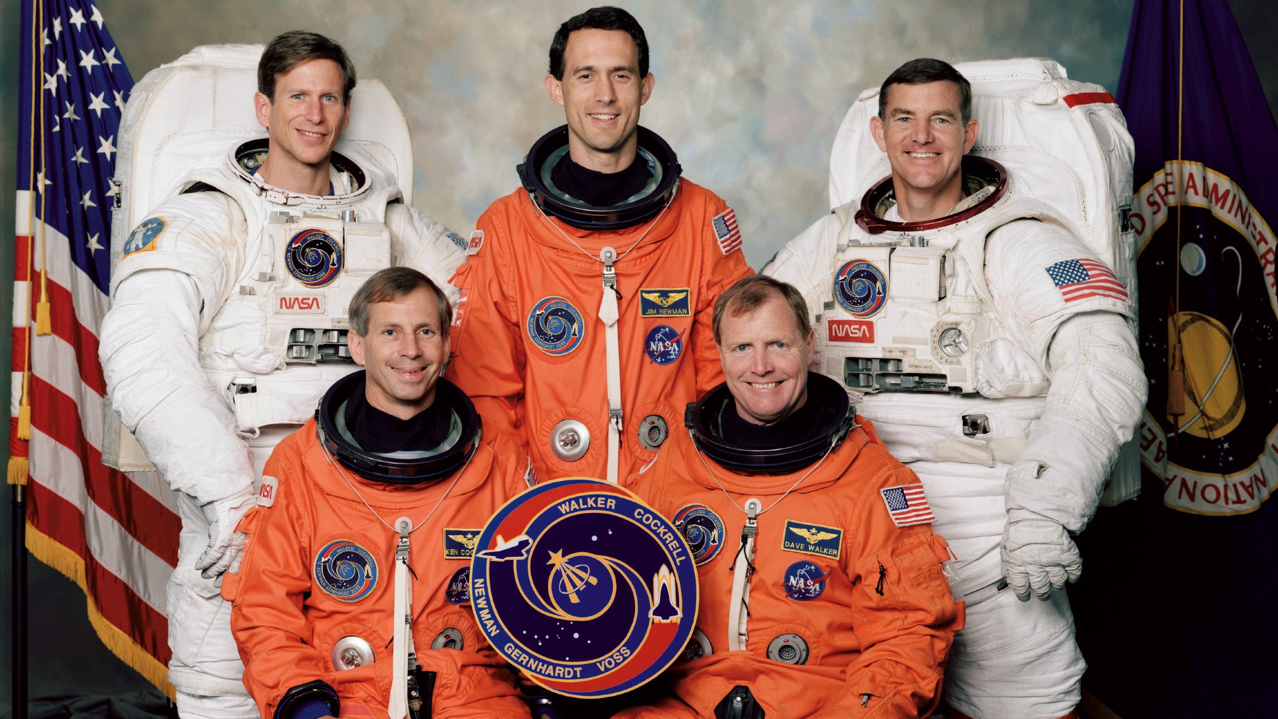 Five astronauts, two in white spacewalking suits and three in orange launch suits, post for an STS-69 NASA shuttle crew portrait.