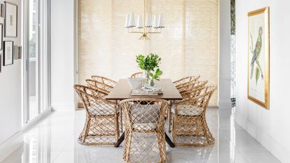 dining room with white walls and glossy white floor tiles with wooden rectangular table and rattan chairs and parrot print on wall