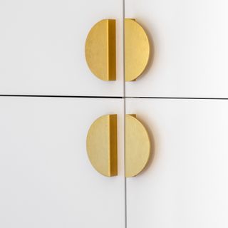 A close-up of white cupboards with half-circle brass handles