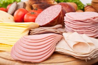 Piles of sliced lunch meat sit on a cutting board.