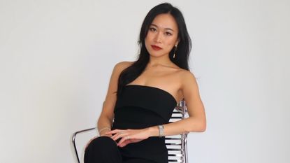 Freja NYC founder, Jenny Lei, sits on metallic chair against white backdrop looking at the camera.