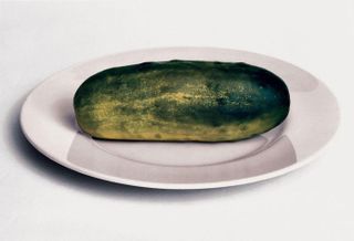 A Large Pickle on a white plate.