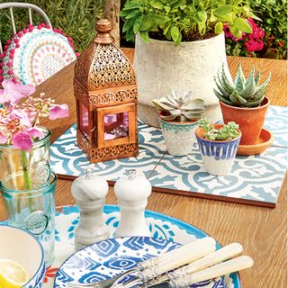 wooden outdoor table with tableware and tiled table protector