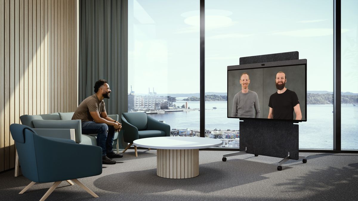 A smiling man sitting on a sofa videoconferencing with two other smiling men on the new Neat Board Pro. 