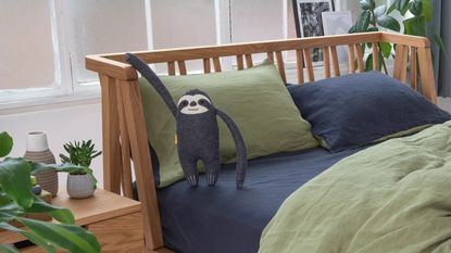 Eve mattress on bed with sloth toy, green and blue bedding, and a side table with plants on it, and a plant to the right