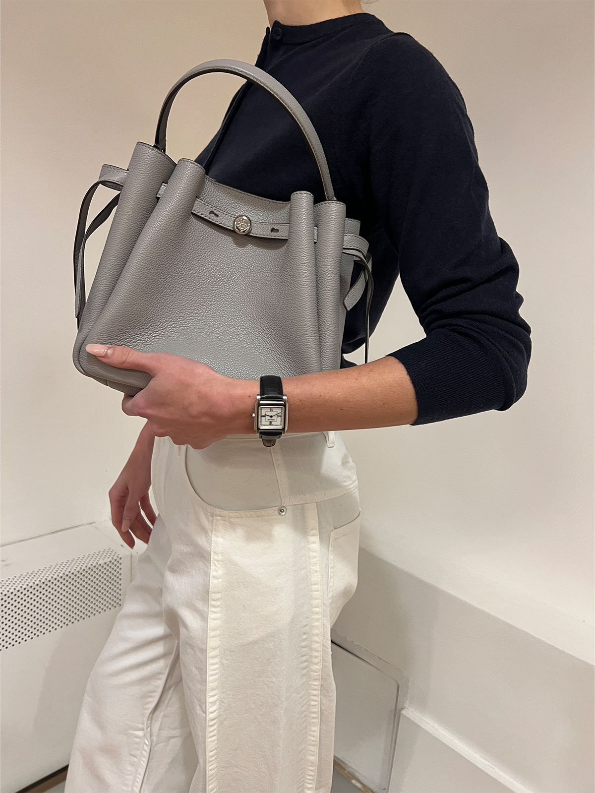 Eliza Huber testing out the Tory Burch Romy Bucket Bag in gray with white Tibi jeans and a navy-blue sweater.