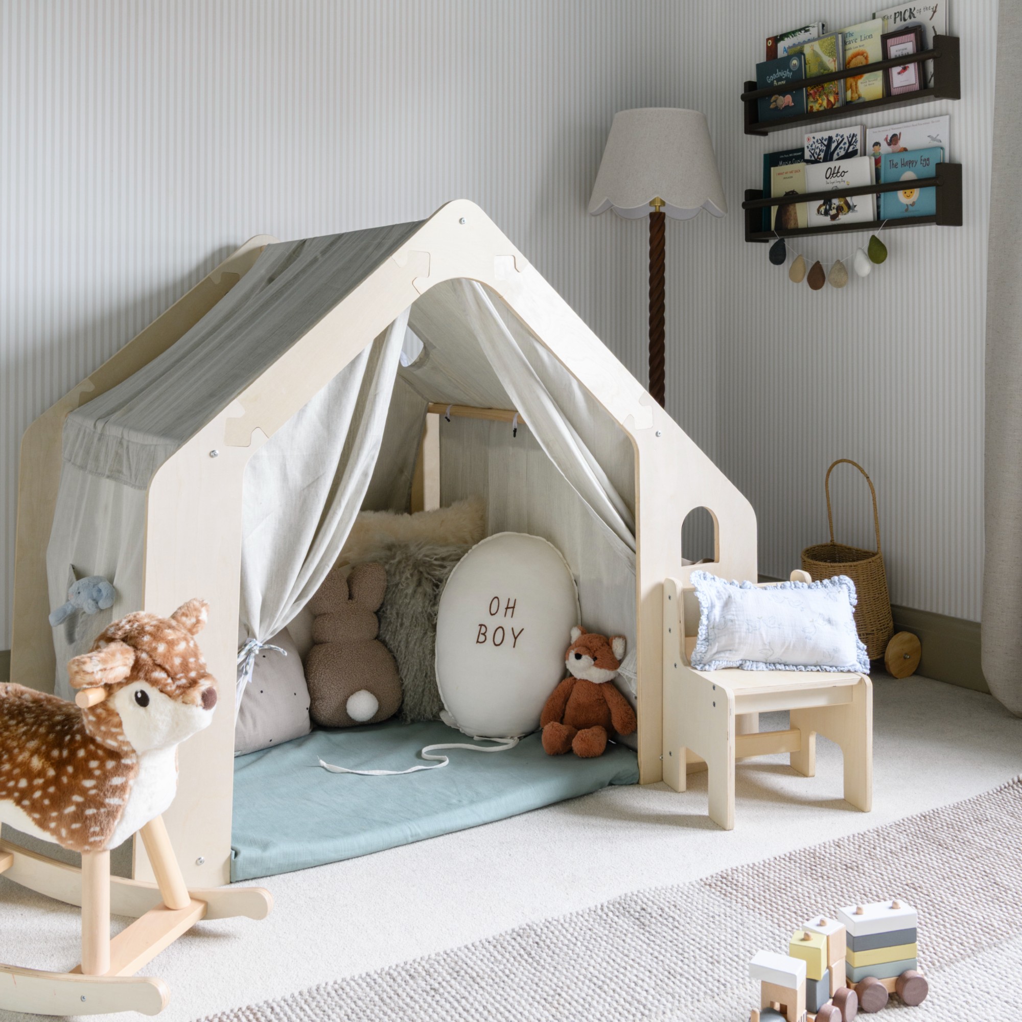 A playroom with a wooden play tent a rocking deer toy and a floor lamp