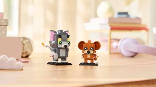 Lego Tom & Jerry Brickheadz figures laid out on a wooden table, with headphones and accessories visible in the background