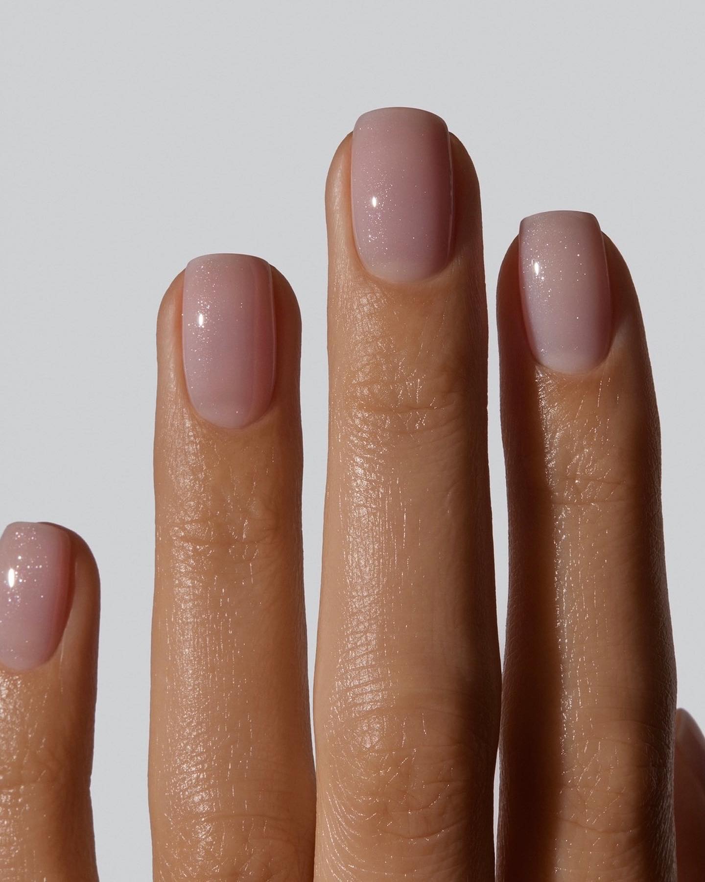 Close-up of short, square nails painted a sheer pink shade with fine shimmer