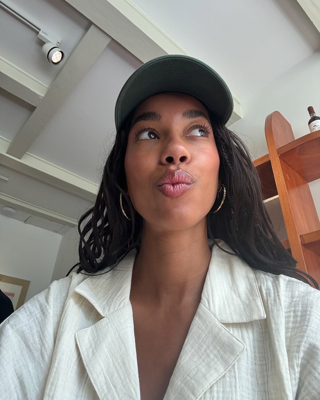 Amaka Hamelijnck wears a cream linen shirt with a green hat
