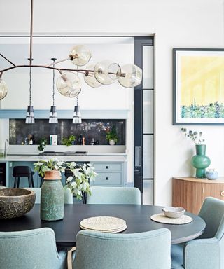 Dining room with view into kitchen, blue color palette, sculptural hanging pendant over dining table, blue dining chairs, blue cabinetry