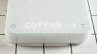 the acaia pearl s coffee scale with an LED screen, on/off, tare button with slip-proof feet and a premium white exterior plastic casing photographed against the tom's guide blue background