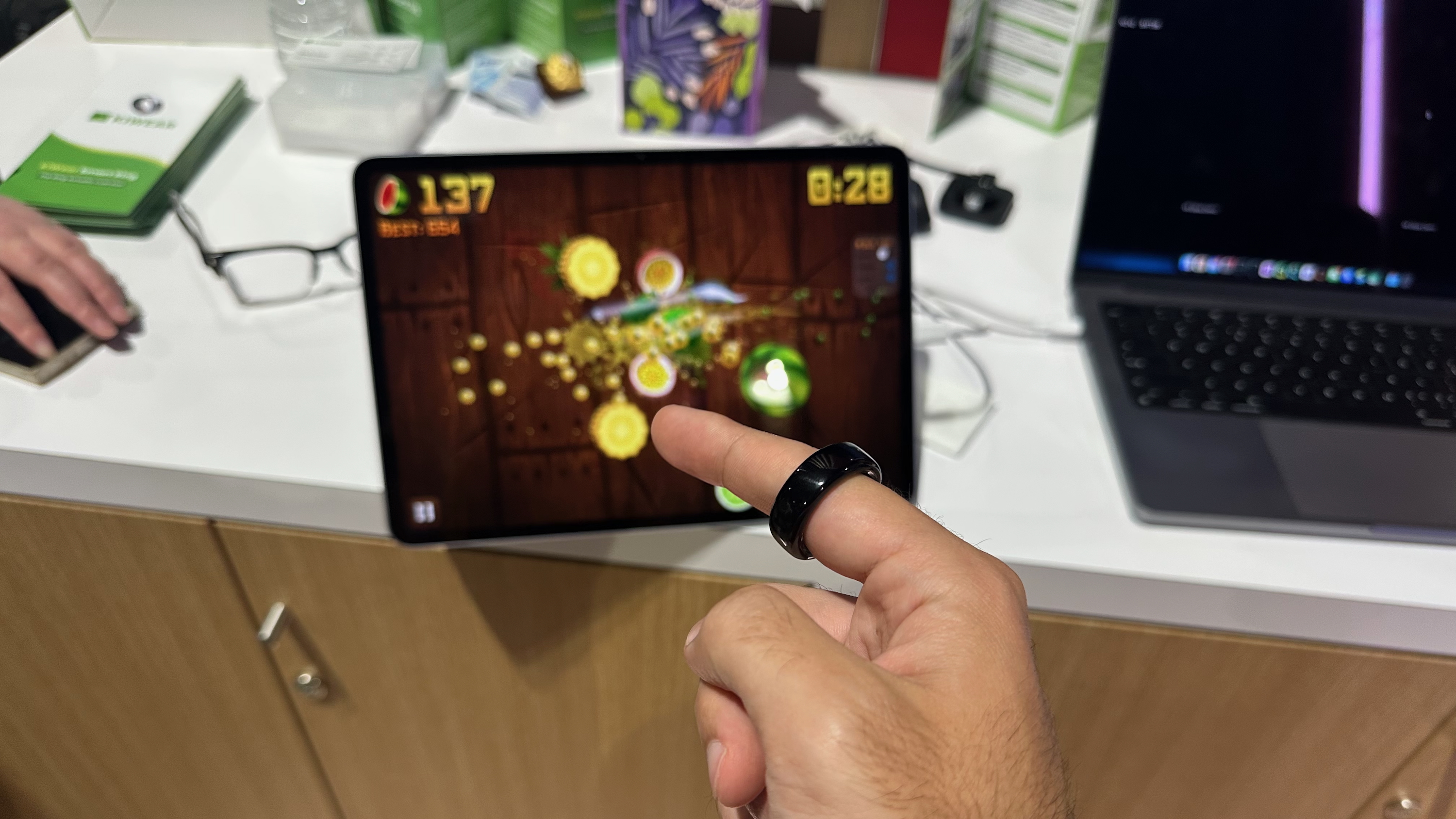 The author wearing a Kiwear smart ring capable of gesture controls, using it to slice fruit in Fruit Ninja on a tablet.