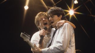 Bryan Adams and Keith Scott share a mic onstage in 1985