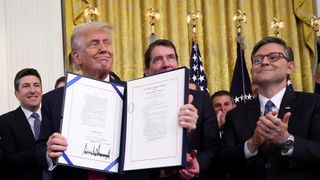 Trump holding the signed GENIUS act while White house officials clap.