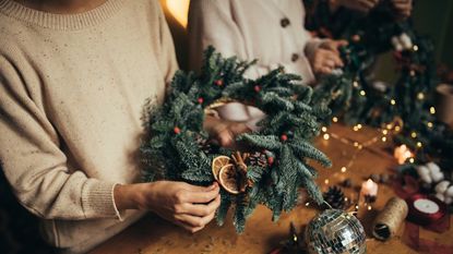 Homemade Christmas wreath being held above wooden crafting table
